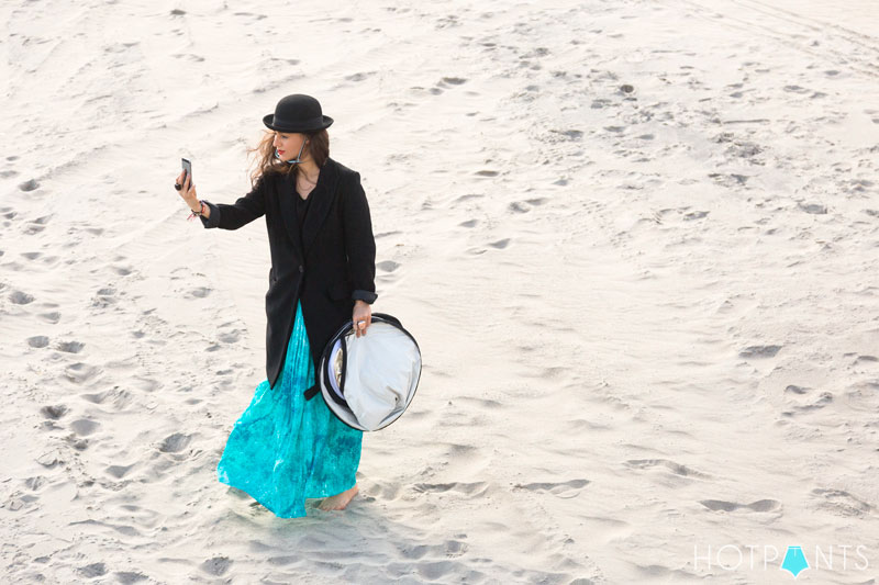 Funny girl jumping sand ocean bowler hat aviators